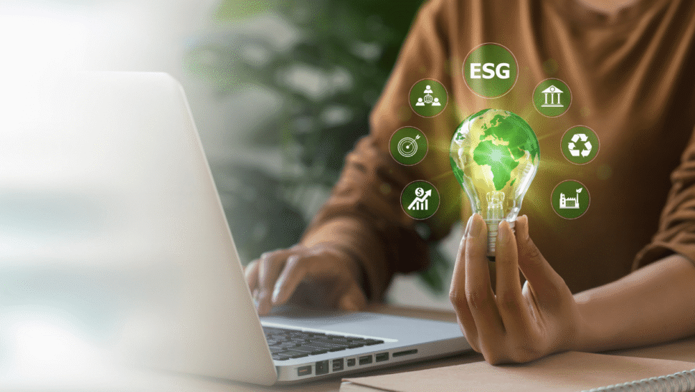Person hält eine Glühbirne am Laptop, umgeben von Icons zu Nachhaltigkeit, Umwelt und Energieeffizienz.